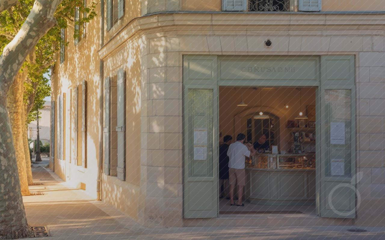 Une boutique ouverte dans une rue de Provence, des clients au comptoir dans la lumière de fin d'après-midi.