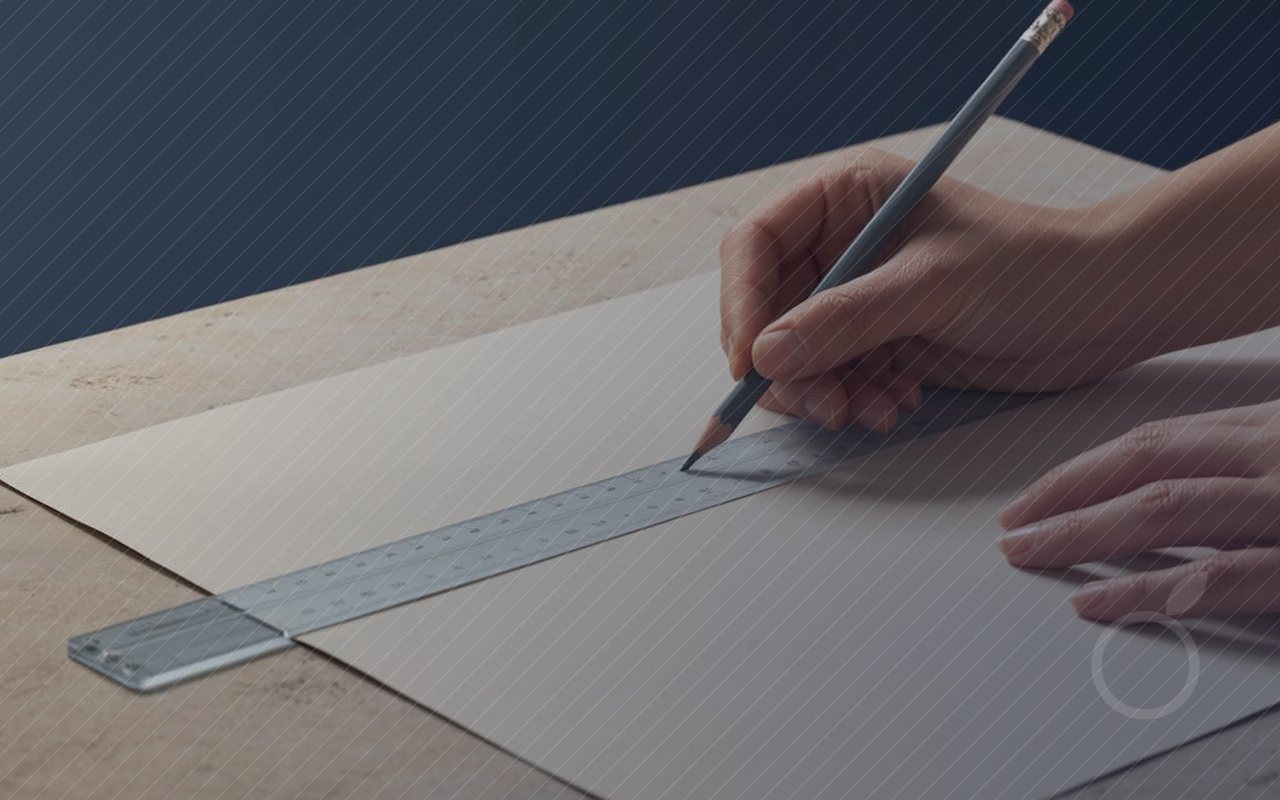 Une main trace une ligne droite au crayon le long d'une règle posée sur une feuille.